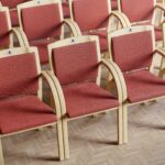 Classic visitor chairs with a high back, red upholstery and a light wooden frame are arranged in a row.